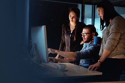 Man presents work on monitor to two female colleagues