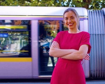 Contact us, girl smiling standing in front of the Luas driving by