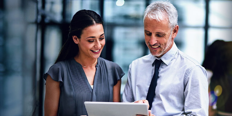 Find a new home for your corporate investment account. Image shows two businesspeople looking at a tablet and smiling