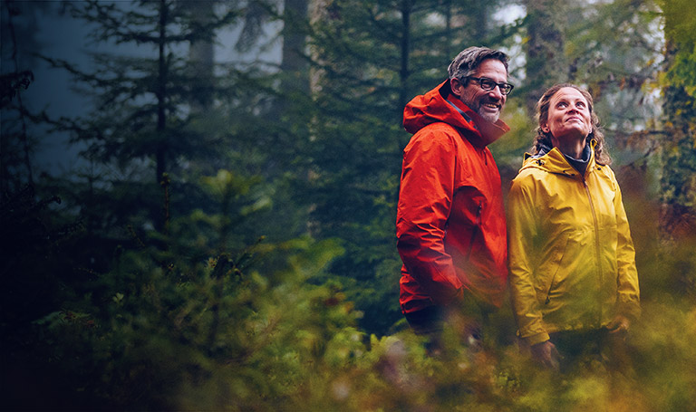We believe the right advice can transform your investment strategy. Image of couple in forest wearing a yellow rain jacket and red rain jacket