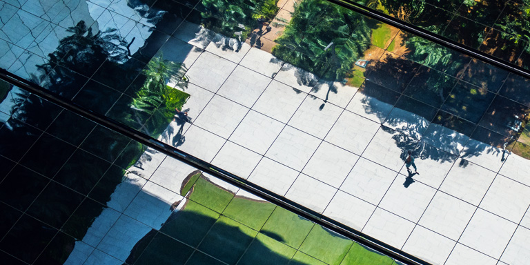 Person walking across corporate garden - grey tiles surrounded by green areas.