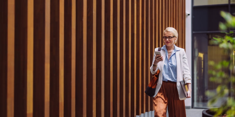 Woman with blonde hair and glasses walks with a wooden slat background