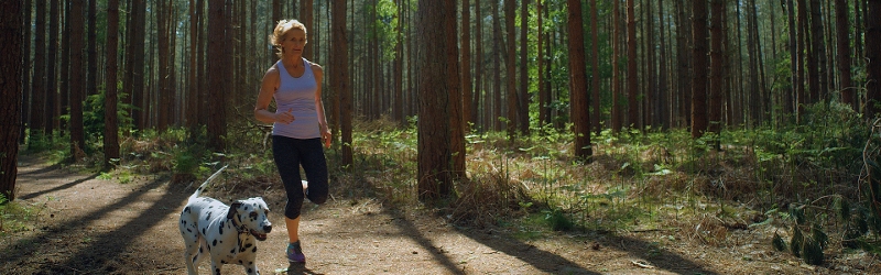 Woman running through the woods with her dog