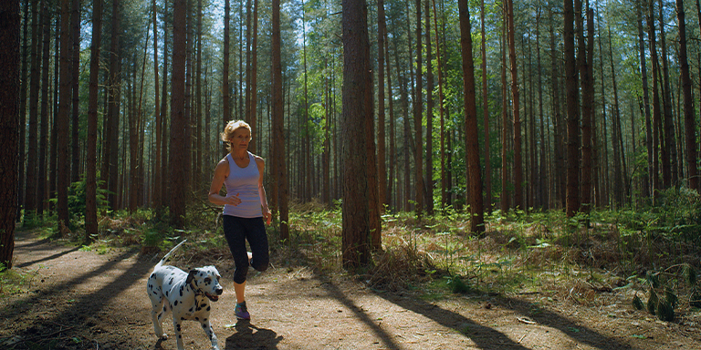 Woman running through the woods with her dog