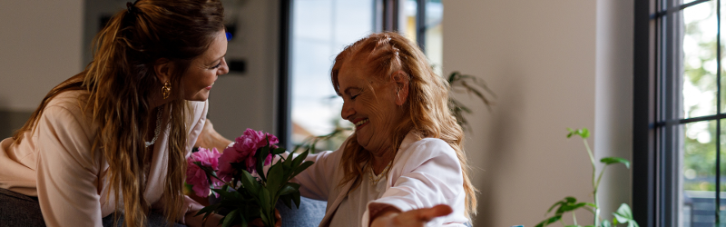 Adult woman gives flowers to elderly mother