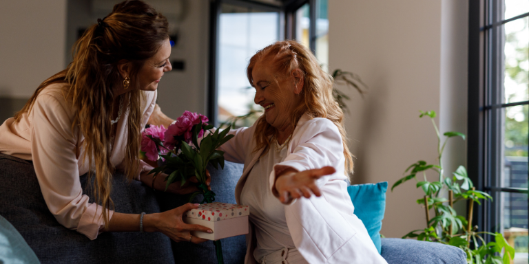 Adult woman gives flowers to elderly mother