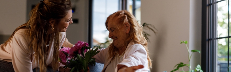 Adult woman gives flowers to elderly mother