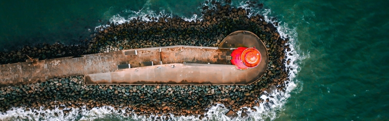 Aerial shot of red poolbeg lighthouse with waves crashing at bottom