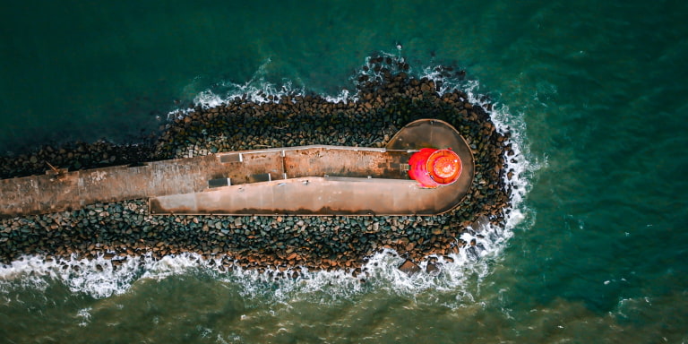 Aerial shot of red poolbeg lighthouse with waves crashing at bottom
