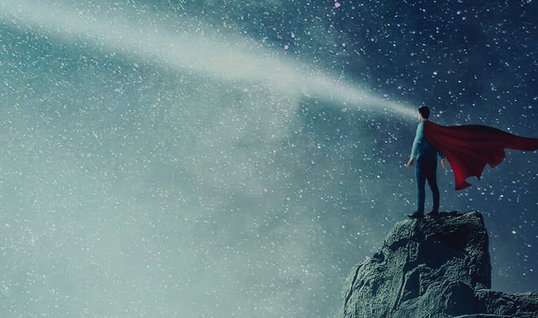 Man in superhero cape standing on edge of cliff with night sky in background