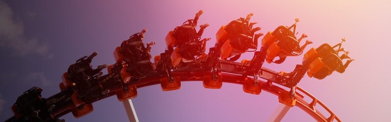 Image of people upside down on a rollercoaster against a pink and blue sky.