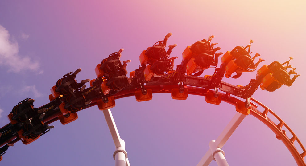 Image of people upside down on a rollercoaster against a pink and blue sky.