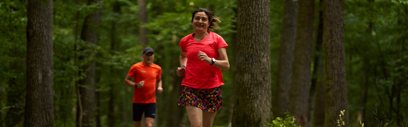Woman and man wearing red running clothes jogging through forest
