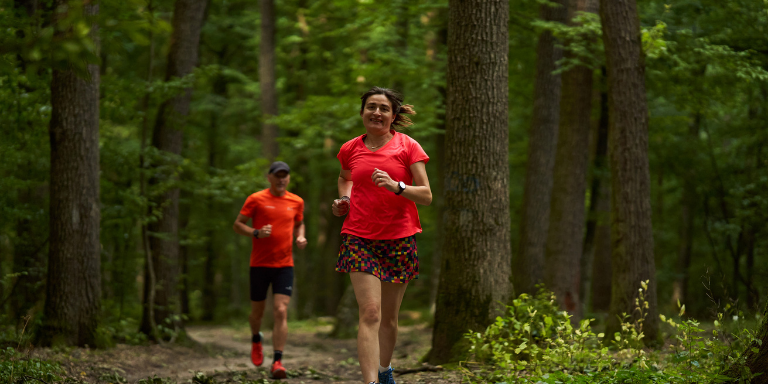Woman and man wearing red running clothes jogging through forest