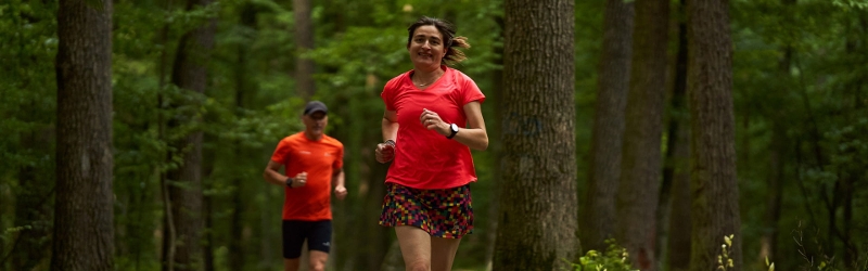 Woman and man wearing red running clothes jogging through forest