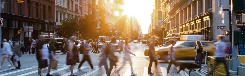 People crossing a busy street in New York with the sun setting in background