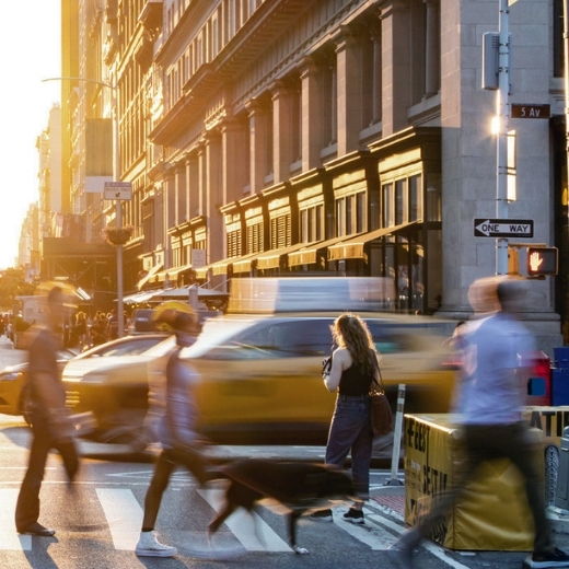 People crossing a busy street in New York with the sun setting in background